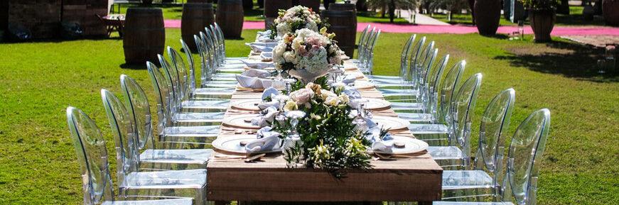 A beautifully set table with elegant tableware, clear acrylic dining chairs, wooden rustic and floral centerpieces.