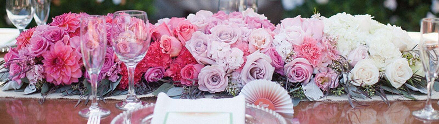 A long floral arrangement on a table with ombre effect from fuschia to white.
