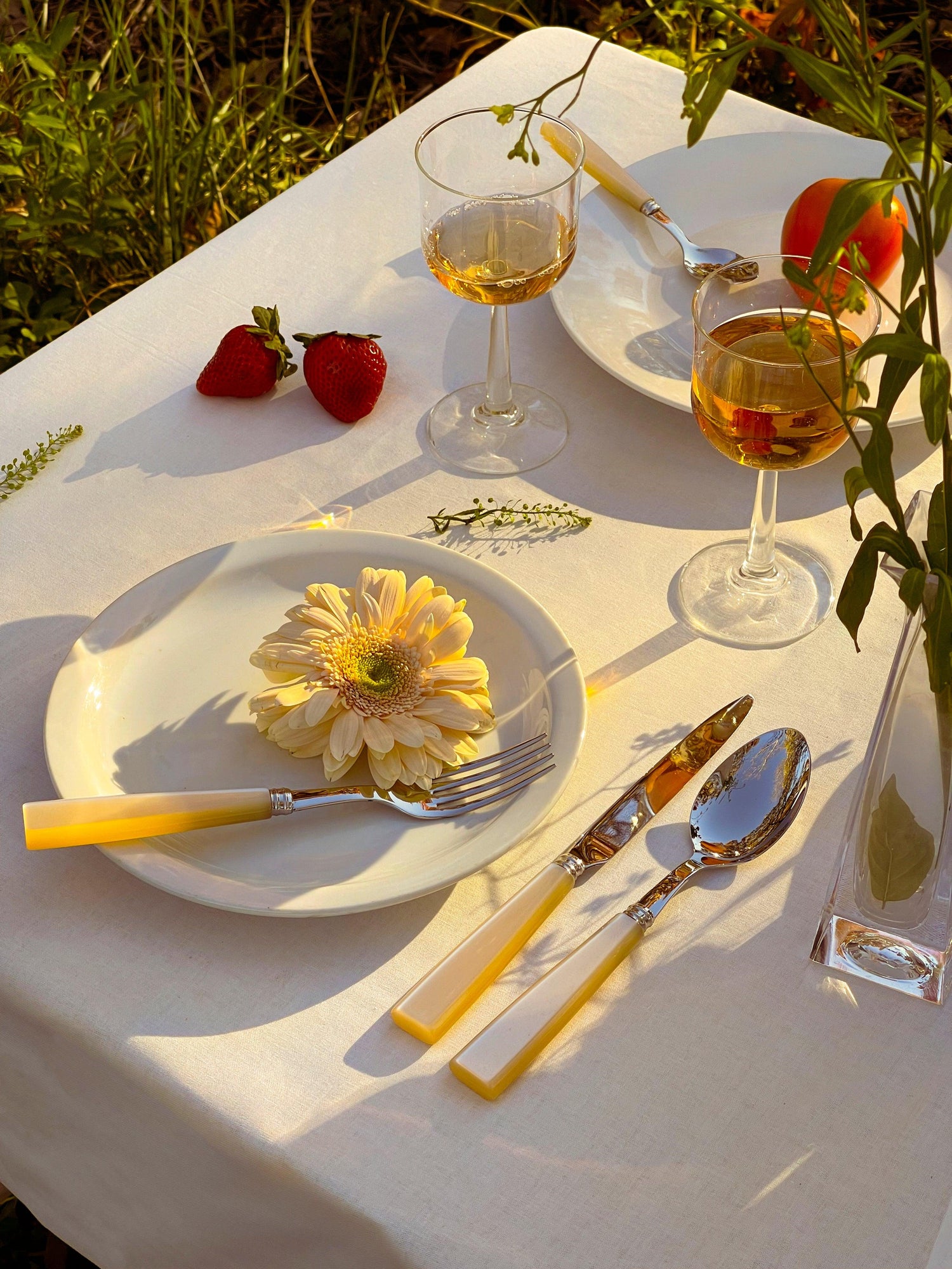A stylish Pearl Cutlery Set of 5 with a plate, fork, and knife on a table with wine glasses.